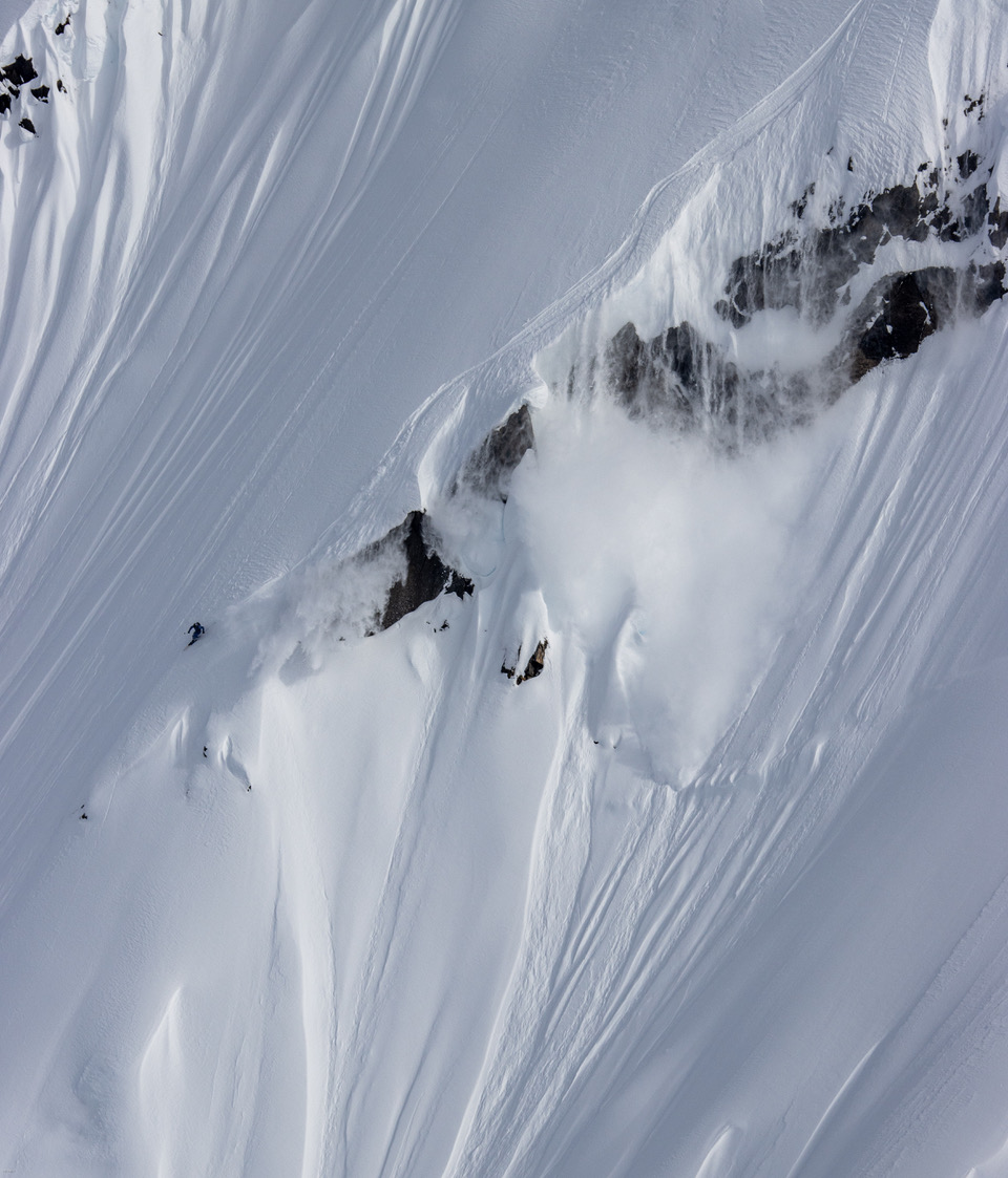 Aerial view of a skier riding a steep, snow-covered spine between exposed rock